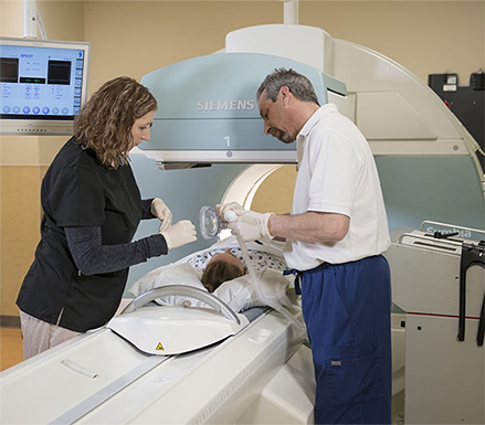 Two Medical Professionals standing next to a patient who is lying down in an MRI Scanning Machine