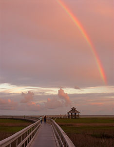 A rainbow in the clouds over two people walking down a long walkway